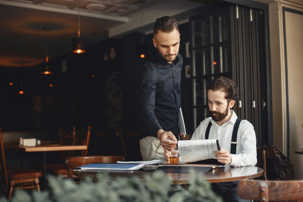 Two men discuss business over documents in a cozy, stylish restaurant.